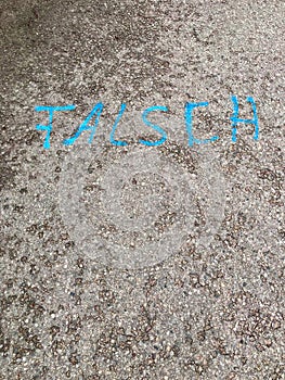 German text Ã¢â¬Å¾FALSCHÃ¢â¬Å wrong painted on asphalt road surface with vibrant bright blue paint. Concrete ground background